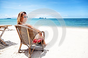 A beautiful young woman in a white bikini sits on a tropical beach. Rest, vacation, resort, beautiful life