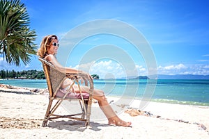 A beautiful young woman in a white bikini sits on a tropical beach. Rest, vacation, resort, beautiful life