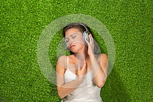 Beautiful young woman in the white dress and headphones lies on the grass and listens music. summer concept. View from the top.