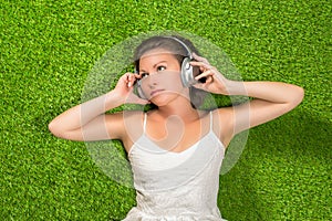 Beautiful young woman in the white dress and headphones lies on the grass and listens music. summer concept. View from the top.