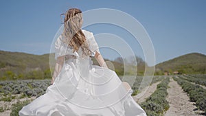 Beautiful young woman in white dress runs across field. Action. Woman's hair and dress flutter beautifully while running