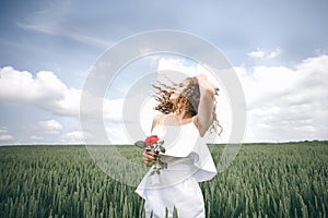 A Beautiful Young Woman In The White Dress Standing In The Field With Rose In Her Hand