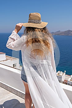 Beautiful young woman in white dress straw hat on white terrace balcony of house or hotel with Sea View