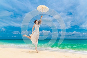 Beautiful young woman in white dress with umbrella on a tropical beach