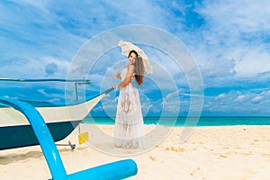 Beautiful young woman in white dress with umbrella on a tropical beach