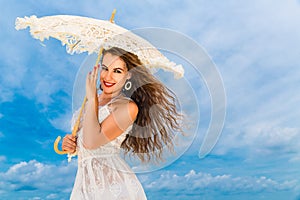 Beautiful young woman in white dress with umbrella on a tropical beach