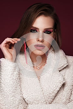 A beautiful young woman in a white fur coat with bright pink make-up and earrings. Beauty face.