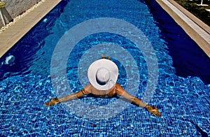 Beautiful young woman in white hat on the pool