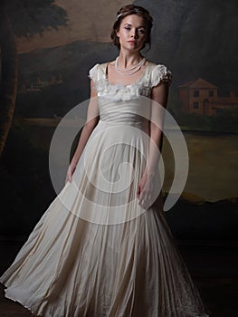 Beautiful young woman in a white long dress in the style of the 19th century.