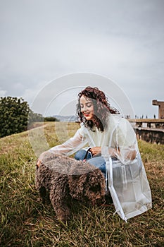 A beautiful young woman with a white rain jacket petting her Spanish water dog in a rainy day in the north of Spain. The dog is