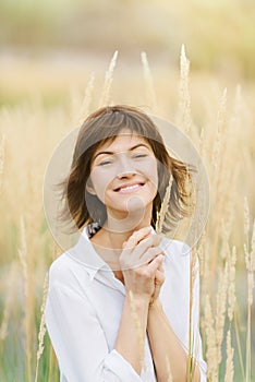 Beautiful young woman in a white shirt smiling standing against a background of tall yellow grass