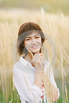 Beautiful young woman in a white shirt smiling standing against a background of tall yellow grass