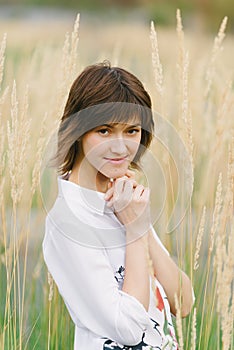 Beautiful young woman in a white shirt smiling  standing against a background of tall yellow grass