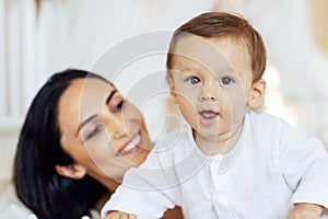 A beautiful young woman in a white top and black leggings holds her little son in a black short