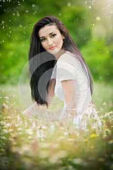 Beautiful young woman in wild flowers field.Portrait of attractive brunette girl with long hair relaxing in nature, outdoor shot