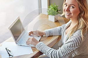 Beautiful young woman working with computer at cafe typing on a keyboard and looking at camera. Top view