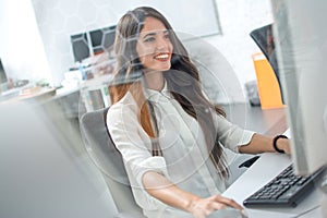 Beautiful young woman working on computer in modern office. Through glass view.