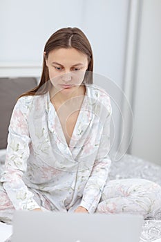 Beautiful Young Woman Working from Home - Female Entrepreneur Sitting on Bed with Laptop Computer, Paperwork from Home. quarantine