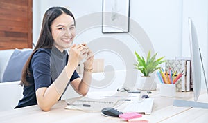 Beautiful young woman working on laptop computer while sitting at the living room. Drinking coffee