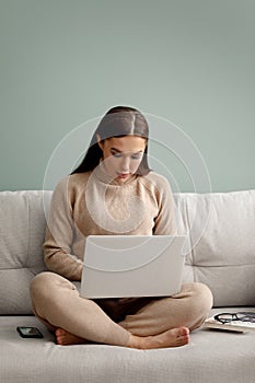 Beautiful young woman working with laptop on couch. Businesswoman using laptop, managing her business.