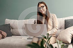 Beautiful young woman working with laptop on couch. Businesswoman using laptop managing her business. Home office during Coronavir