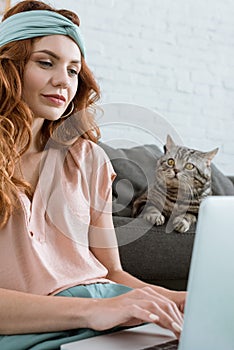 beautiful young woman working with laptop while sitting near her tabby cat