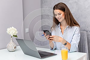 Beautiful young woman working on laptop use phone in the kitchen