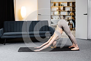 Beautiful young woman working in living room, doing yoga exercise in the room with blue couch, downward facing dog pose, sun