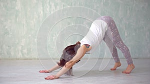 Beautiful young woman working out indoors, doing yoga exercise in the room with white walls, downward facing dog pose