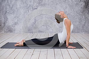 Beautiful young woman working out indoors, doing yoga exercise in the room with white walls, downward facing dog pose