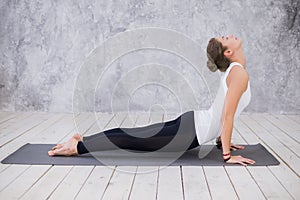 Beautiful young woman working out indoors, doing yoga exercise in the room with white walls, downward facing dog pose