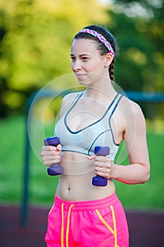 Beautiful young woman working out with weights outdoors. Active girl working out with small dumbbells in the park