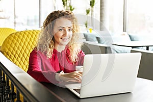 Beautiful young woman working remotely on her fashionable laptop at hipster coffee shop. Happy female freelancer with trendy wrist