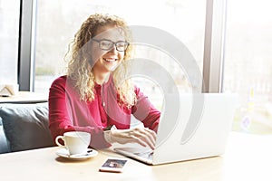 Beautiful young woman working remotely on her fashionable laptop at hipster coffee shop. Happy female freelancer with trendy wrist