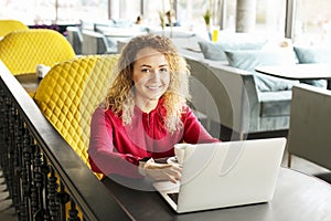 Beautiful young woman working remotely on her fashionable laptop at hipster coffee shop. Happy female freelancer with trendy wrist