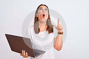 Beautiful young woman working using computer laptop over white background amazed and surprised looking up and pointing with