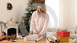 Beautiful young woman wrapping Christmas gift at home