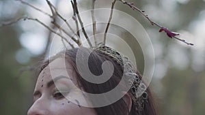 Beautiful young woman with wreath of branches on the head in costume of forest fairy or dryad dancing in forest showing