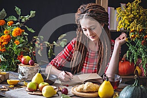 Beautiful young woman writes autumn dreams in a notebook. Fall table with flowers. Concept of autumn romantic mood