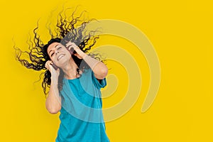 Beautiful young woman on yellow colored background listens to music and shakes her head while dancing