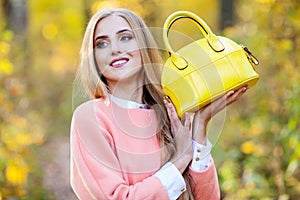 Beautiful young woman with yellow fashionable bag in hands on autumn nature