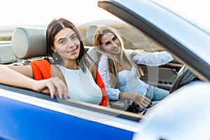 Beautiful young women in sunglasses driving on cabriolet, looking away and having fun