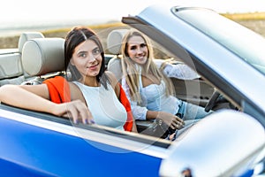 Beautiful young women in sunglasses driving on cabriolet, looking away and having fun