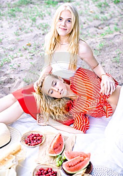 Beautiful young women talking, smiling and gesturing while having picnic outdoors at park.