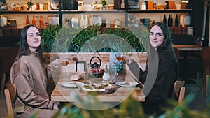 Beautiful Young Women Twins Dine in Restaurant. Sisters are looking at Camera.