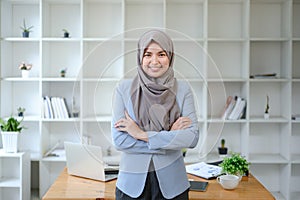 Beautiful young working woman in hijab standing in office, smiling. Portrait of confident muslim businesswoman. Modern