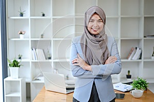 Beautiful young working woman in hijab standing in office, smiling. Portrait of confident muslim businesswoman. Modern