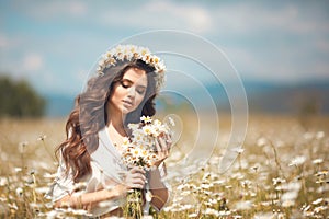 Beautiful young girl with flowers enjoying in chamomile field. Carefree happy brunette woman with chaplet on healthy wavy hair photo