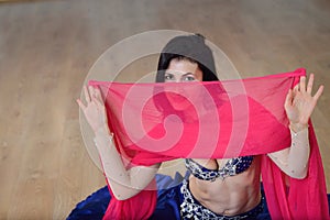 Beautifull caucasian woman in costume for belly-dance is dancing indoors at fitness class covered in silk veil