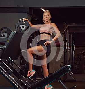 Beautifull fitness woman in sportswear posing near the legs press machine in a gym.